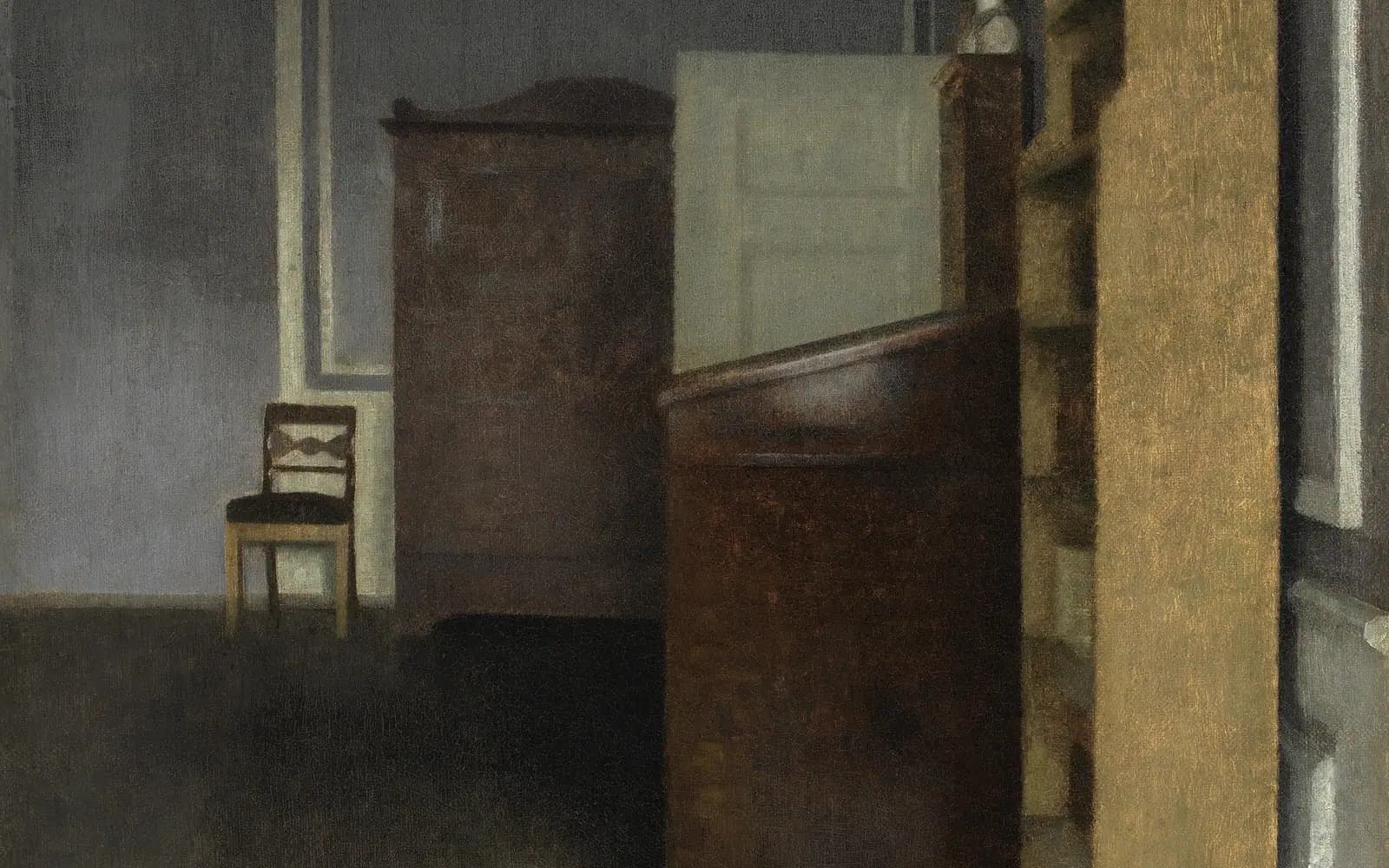 A quiet, dim room painted in greys and browns, with a tall wooden writing desk in the foreground, a dark cabinet behind it and a single wooden chair against a pale wall.