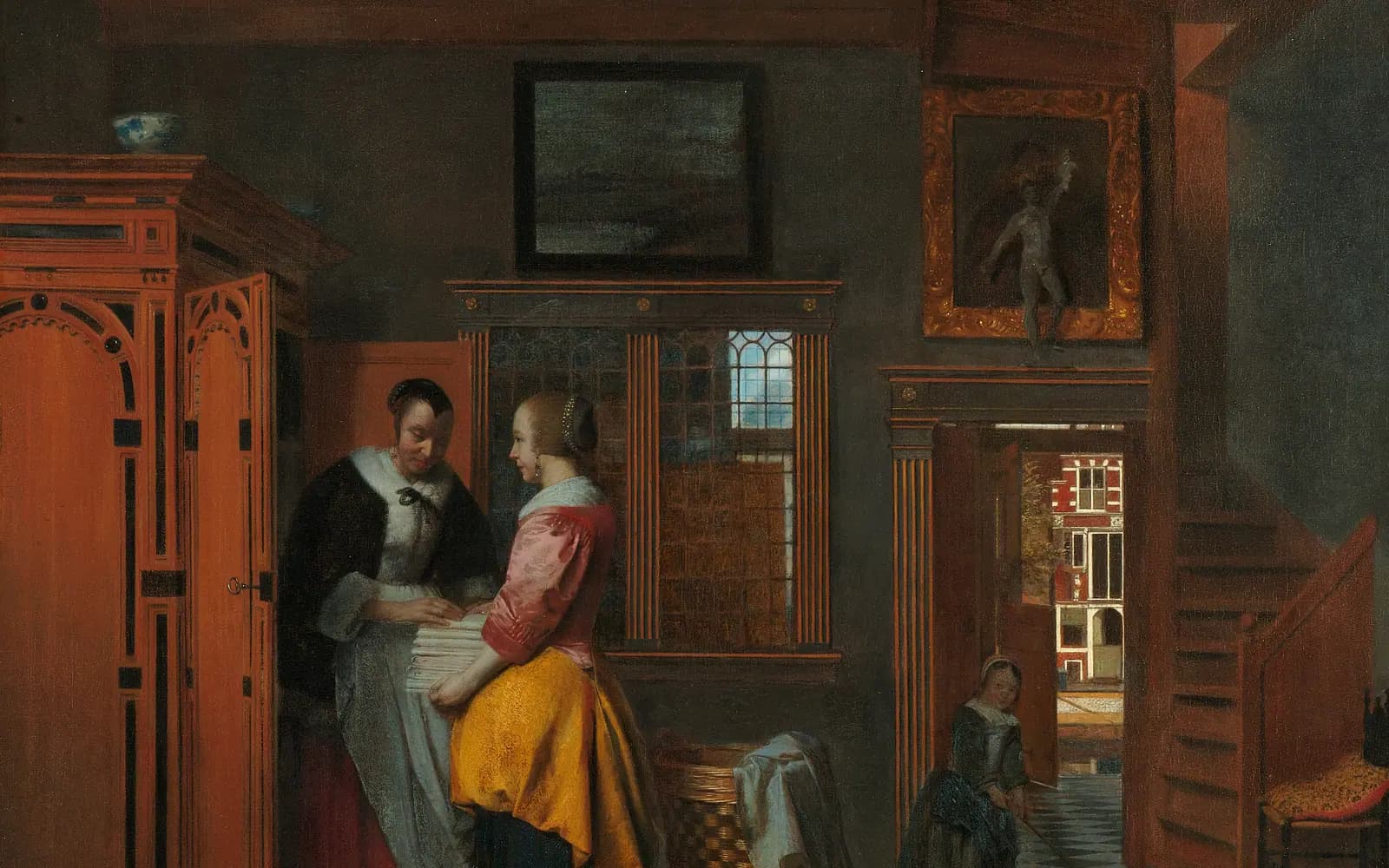 Dutch interior painting of two women stacking folded linen into a tall wooden cupboard while a child plays in a doorway that opens onto a canal street.