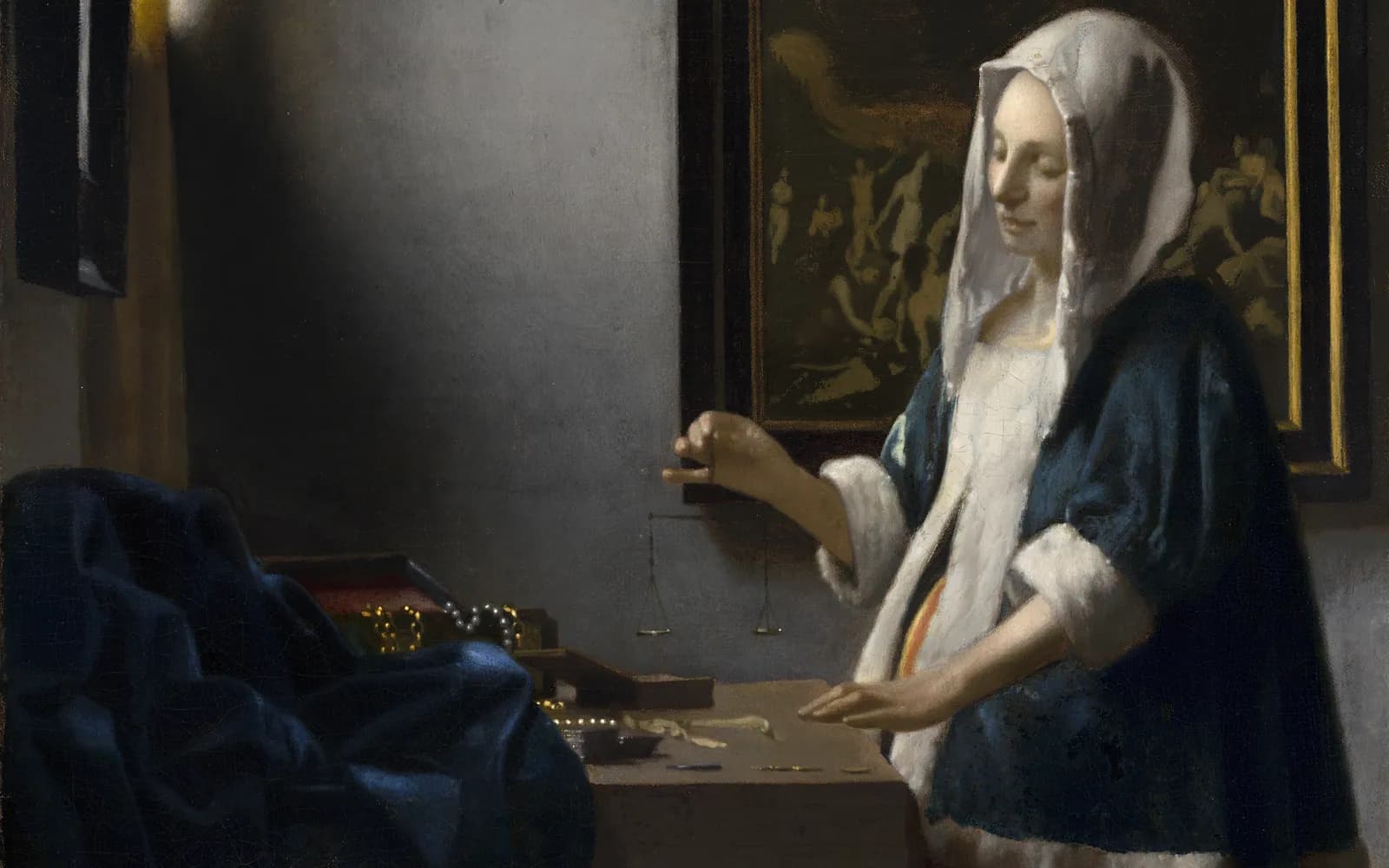 Painting of a woman in a blue fur-trimmed jacket and white headscarf standing at a table by a window, holding a small empty balance scale, with pearls and gold on the table and a dark painting on the wall behind her.